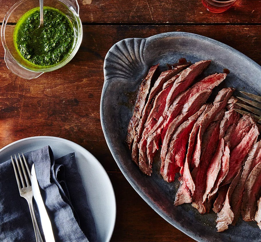 Sliced flank steak on platter with green sauce in a bowl